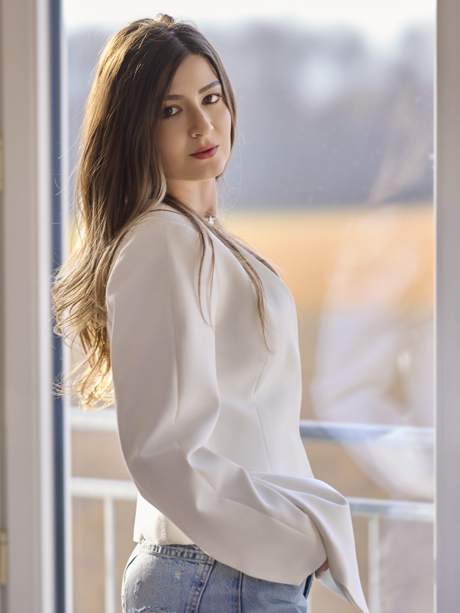Modernes Bewerbungsbild einer Frau in weißer Bluse im hellen Fensterlicht.