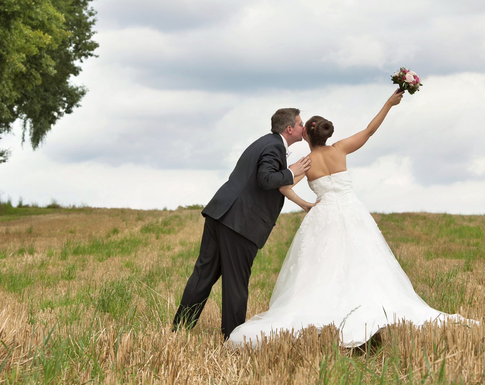 Hochzeitspaar im warmen Spätsommerlicht zwischen Feldern.