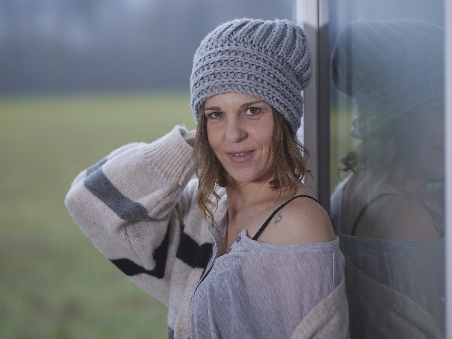 Natürliches Einzelportrait einer Frau mit weicher Spiegelung am Fenster.